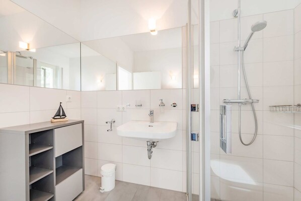 A modern bathroom with a glass shower enclosure, a white sink, and a vanity with open shelves.