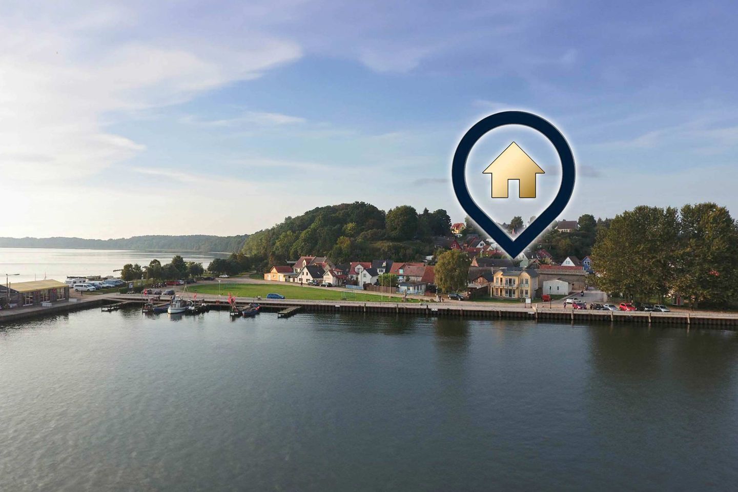 Un pueblo a orillas del lago con un puerto deportivo, casas y un icono de casa destacado.