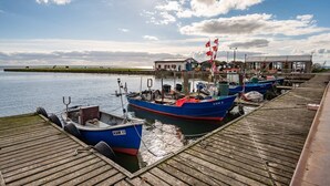 Une jetée où sont amarrés des bateaux, un bâtiment avec un toit rouge et un ciel dégagé.