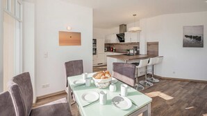 Une cuisine moderne dotée d’un îlot central, d’un coin repas avec une table dressée pour deux personnes, et offrant une vue sur l’espace de vie adjacent.