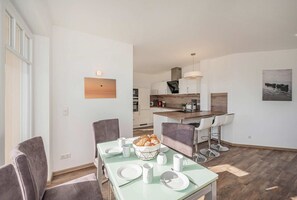 Eine moderne Küche mit Kochinsel, ein Essbereich mit Tisch für zwei Personen und Blick auf den angrenzenden Wohnraum.