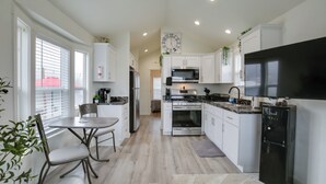 A modern kitchen with white cabinets, a black refrigerator, a microwave, and an oven. There is a dining table with chairs and a window with blinds. - Private Pond & Dock! Cozy Cabin in Southern Oregon (Oakland)