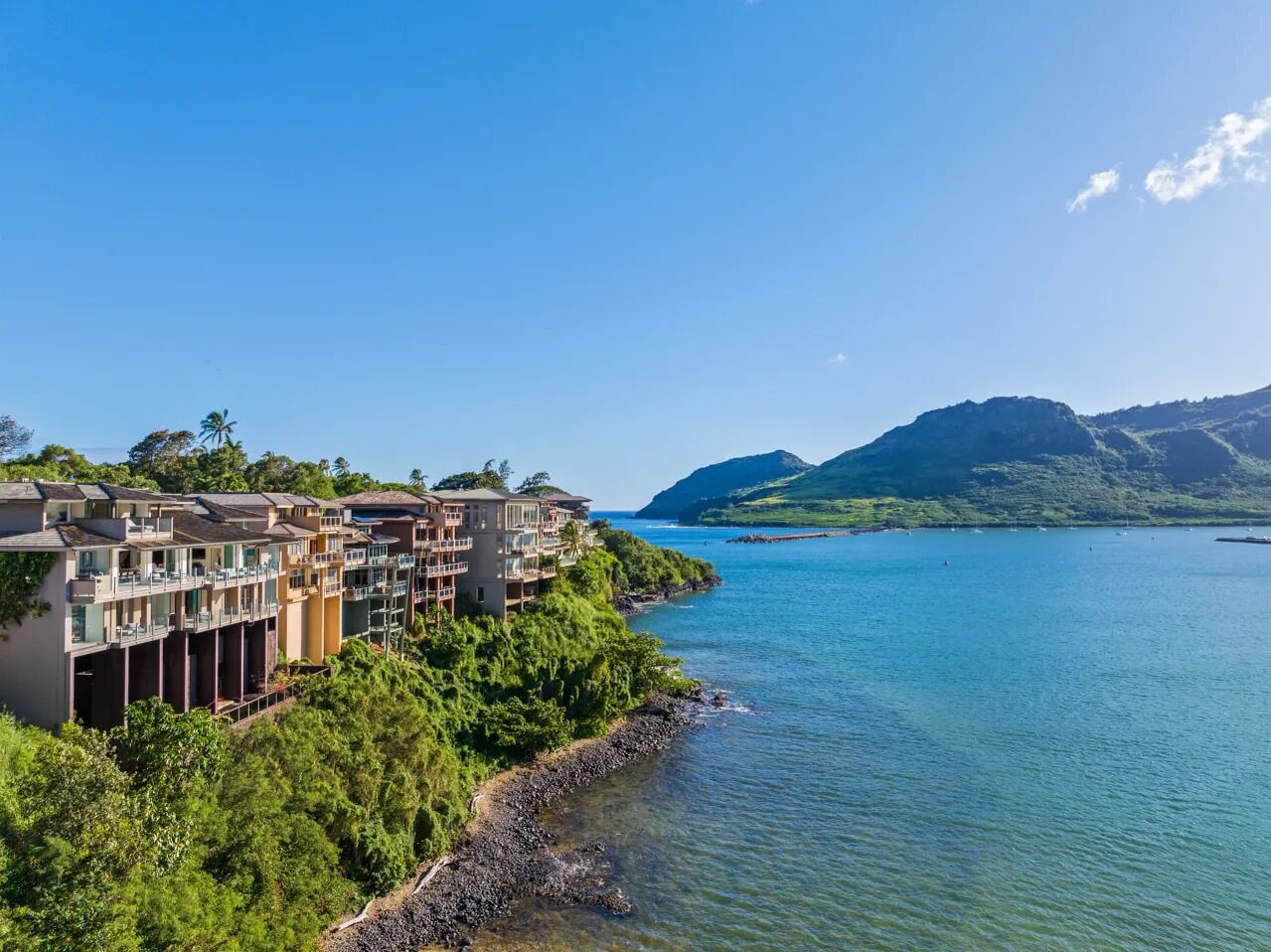 A coastal hotel with multiple balconies overlooking a clear blue sea and lush greenery.