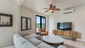 A living room with a sofa, armchair, TV, and ceiling fan. - Oceanview Kauai Retreat | Balcony & Beach Access (Lihue)