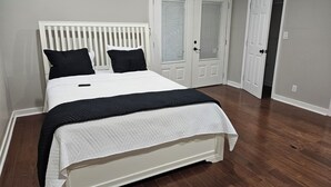 Quarto com cama branca, almofadas preta e branca, manta acolchoada e cabeceira branca.