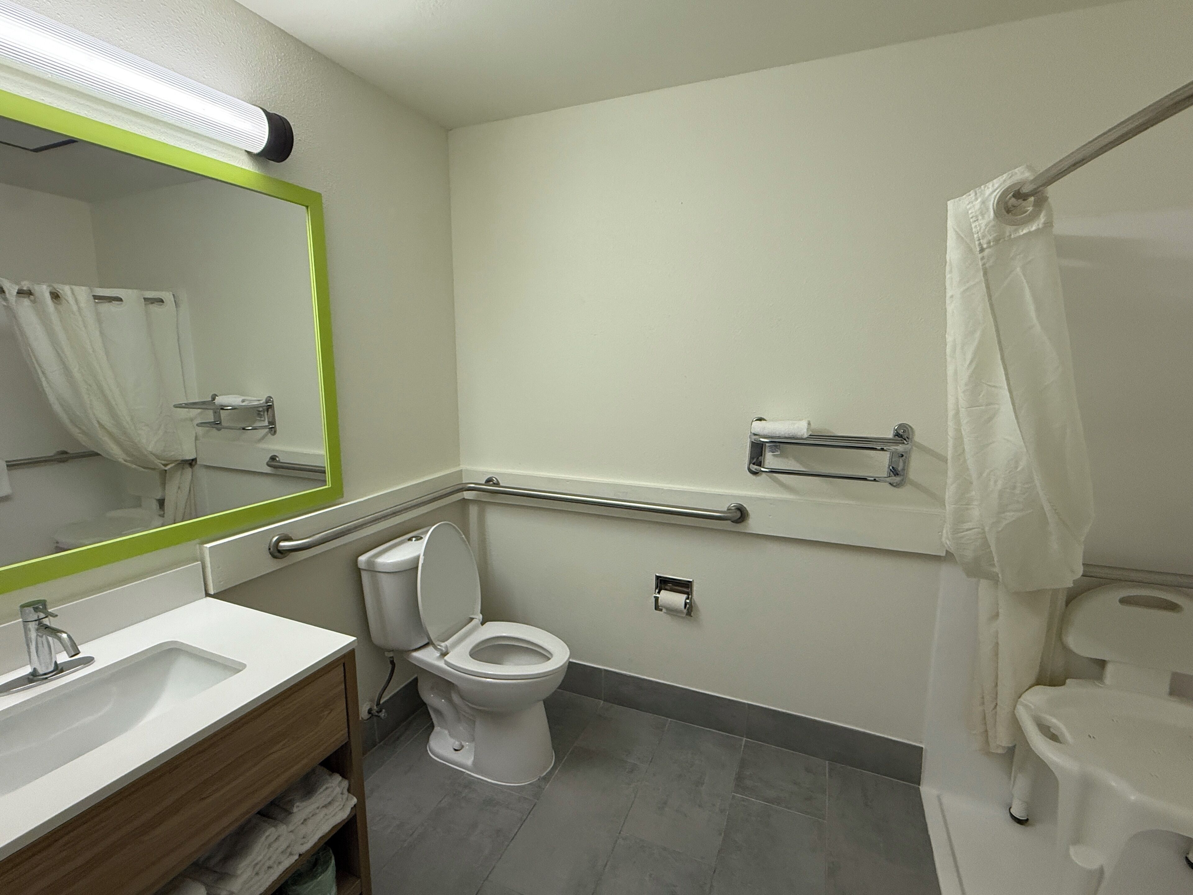 Et badeværelse med hvid vask, spejl, toilet og gelænder.