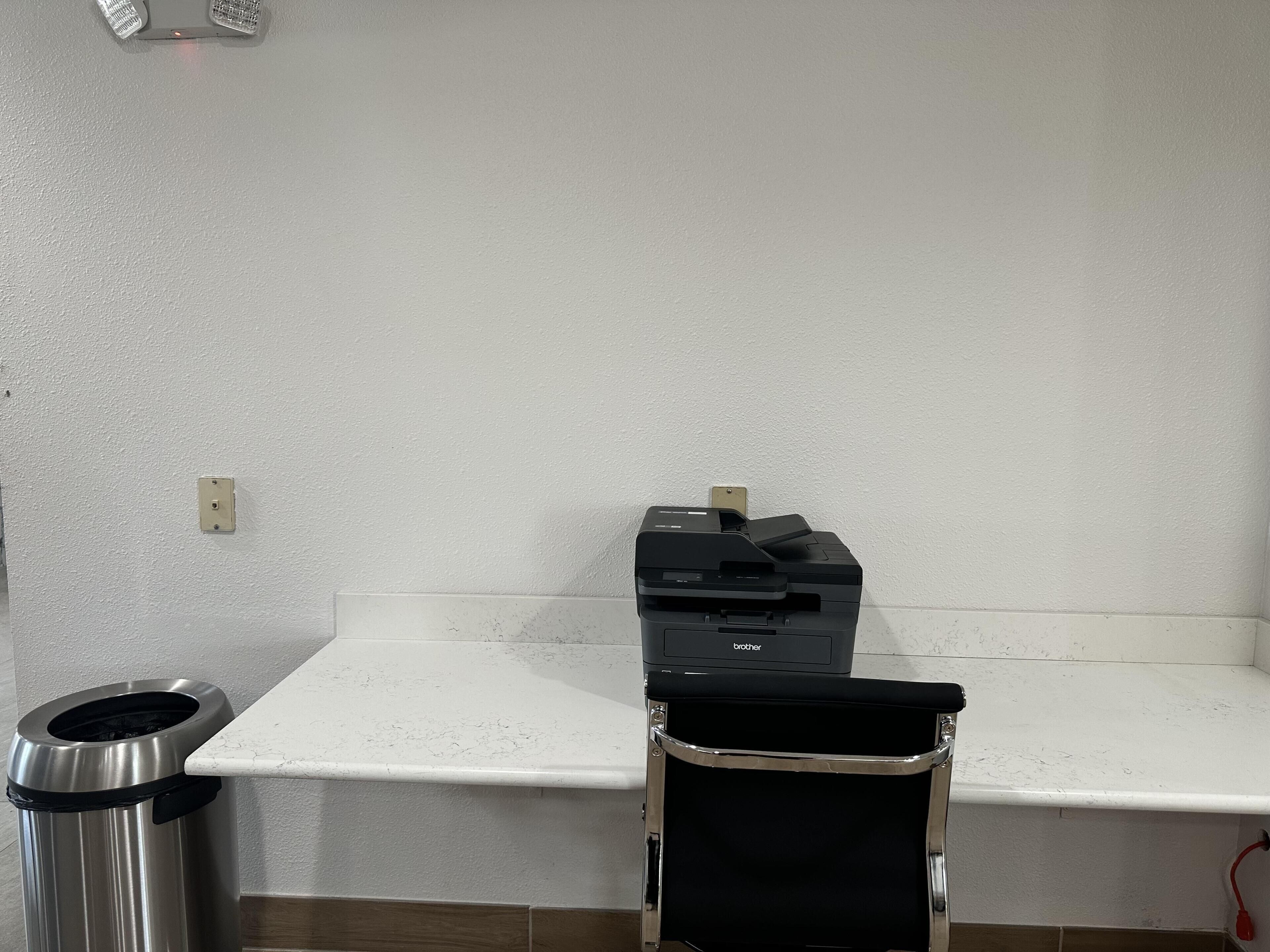 A corner of a room with a white countertop, a trash can, and a printer on a shelf.