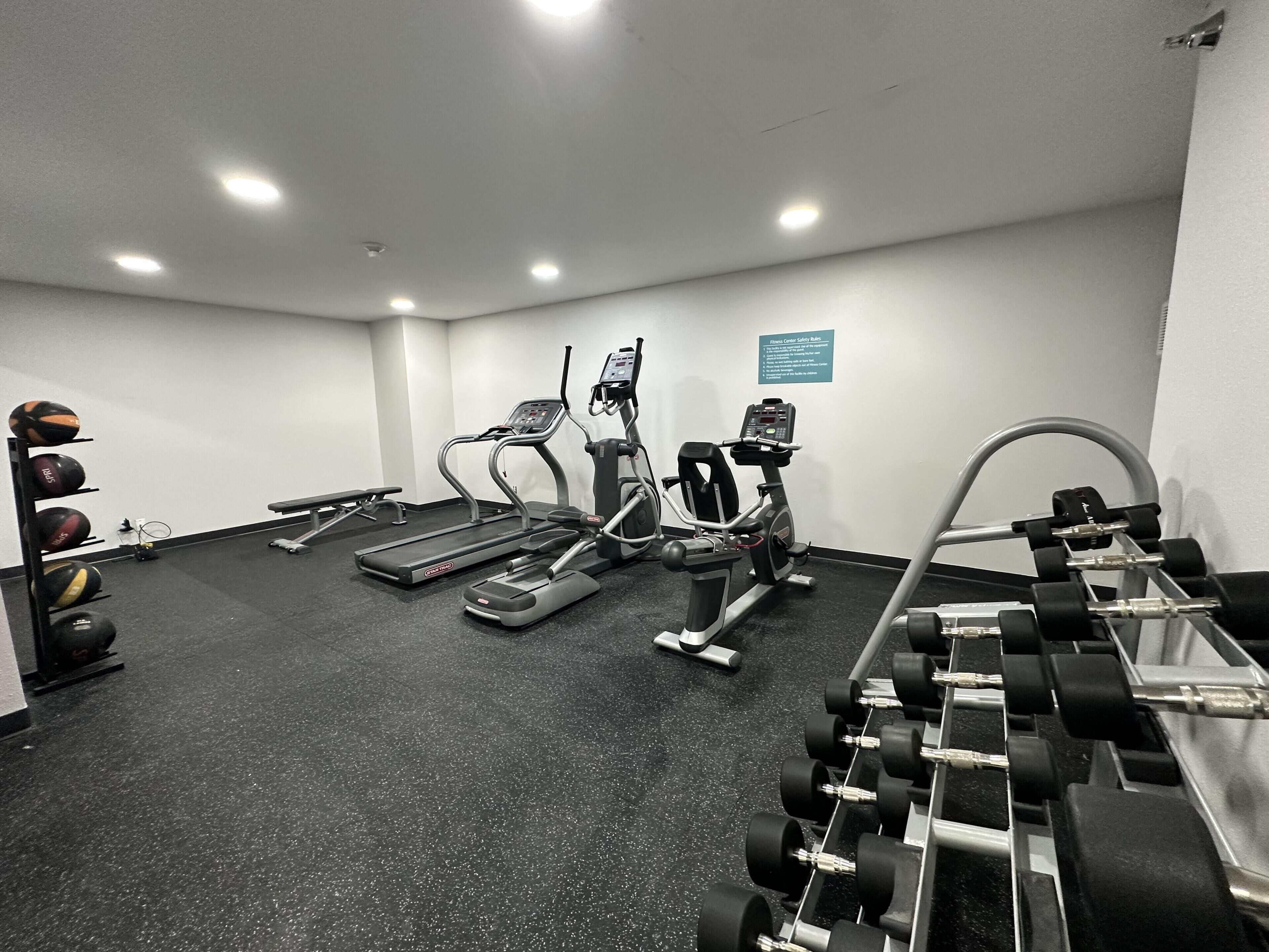 Un gimnasio con cintas de correr, elípticas y un estante con mancuernas.