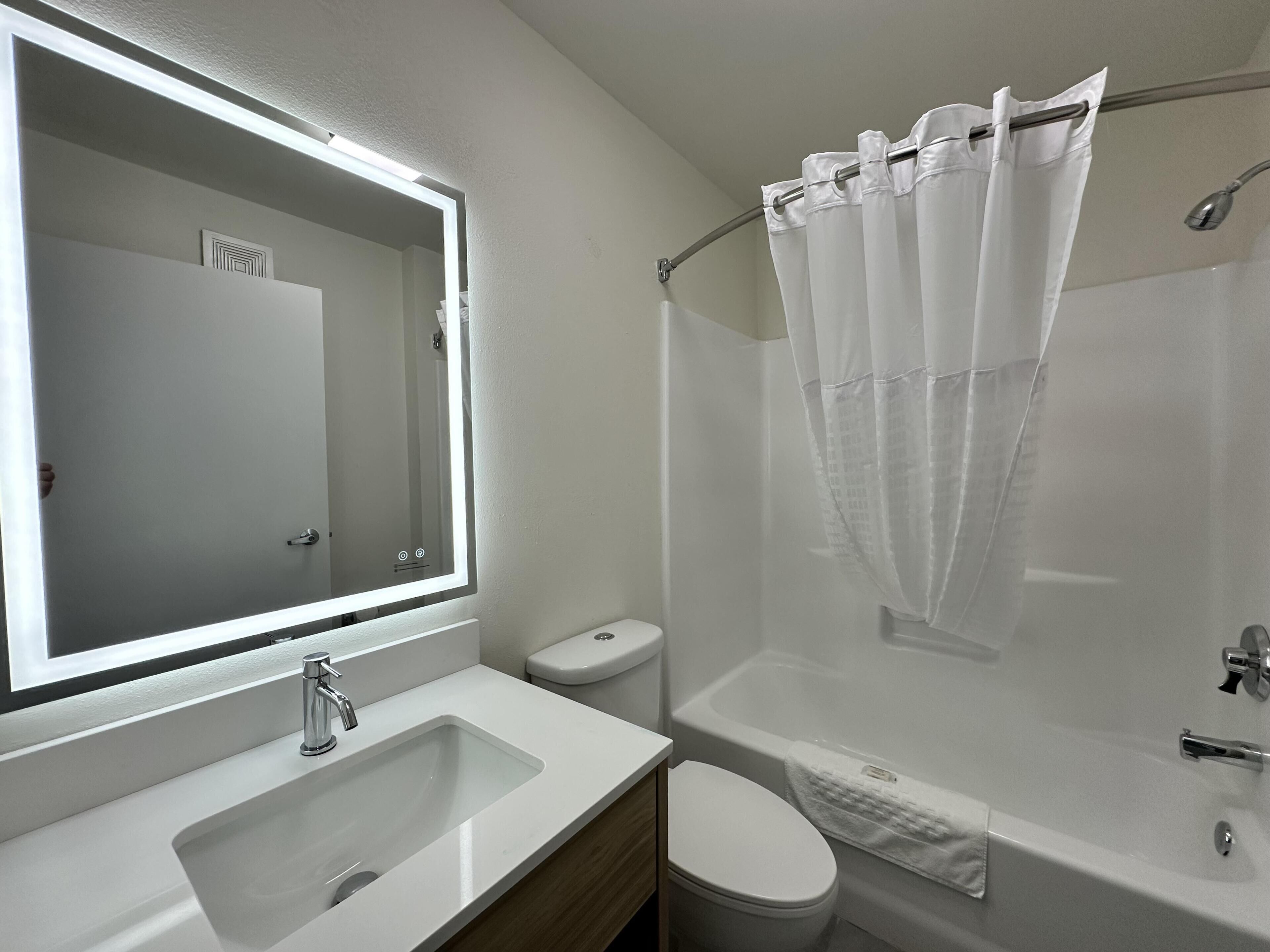 Un baño con lavamanos blanco, espejo, inodoro y bañera con cortina de ducha.