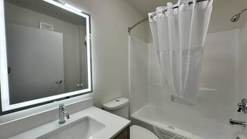 Un baño con lavamanos blanco, espejo, inodoro y bañera con cortina de ducha.
