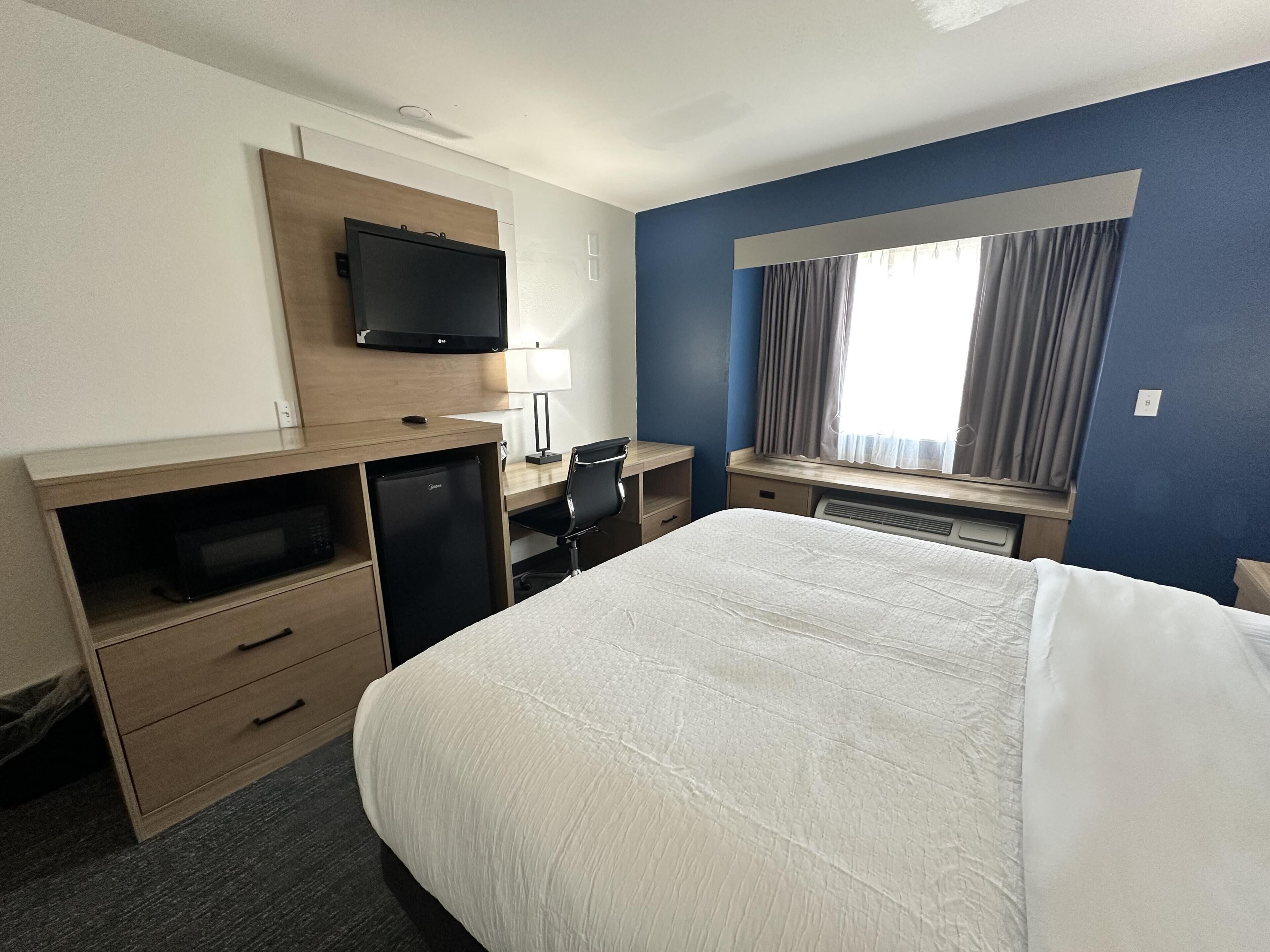 Une chambre d’hôtel avec un lit, un bureau, une télévision et une fenêtre avec des rideaux.