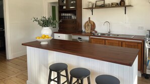 Een keuken met een houten kookeiland, barstoelen, een inbouwoven en een hanglamp.