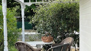 Een overdekt terras met rieten meubels en een tafel, omringd door groen.