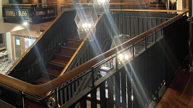 Een modern interieur met een houten trap, metalen leuning en hangende geometrische lampen.