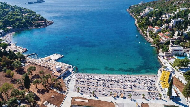 Vista aérea de un pueblo costero con puerto deportivo, playa y edificios residenciales.