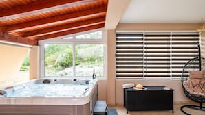 Un jacuzzi en un espacio exterior cubierto con vistas a zonas verdes, un sofá de mimbre y una silla colgante.