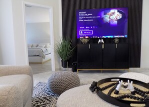 A modern living room with a TV displaying a cooking show, a sofa, a decorative tray, and a plant.