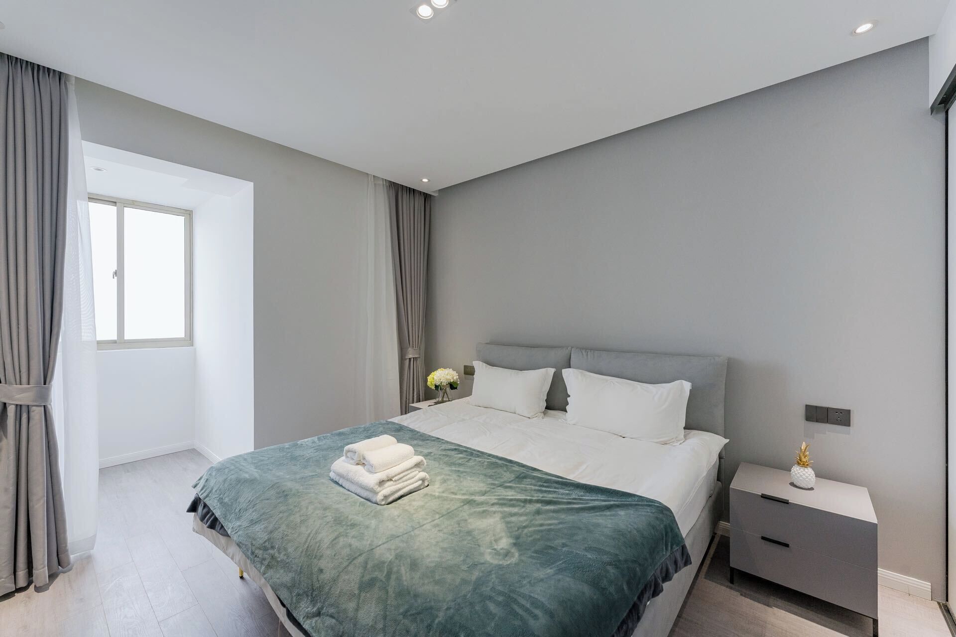 A modern bedroom with a large bed, grey curtains, a nightstand, and a window.
