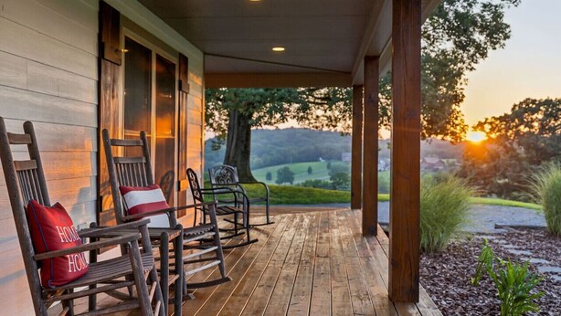 A wooden porch with rocking chairs and a view of a sunset over a landscape.