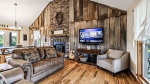 A cozy living room with a stone fireplace, a television, and a guitar.