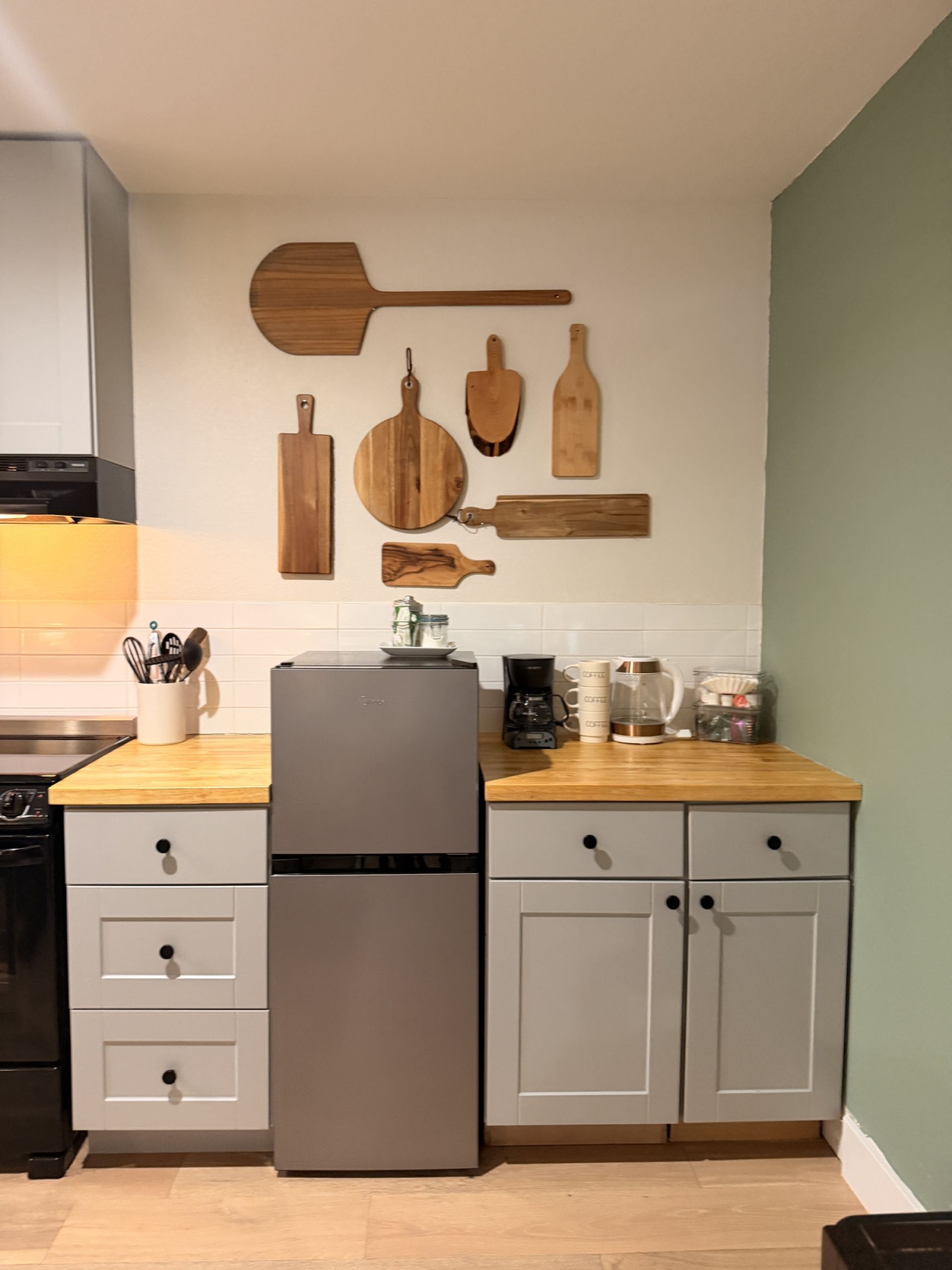 A kitchen with a refrigerator, coffee maker, and various wooden utensils on the wall.