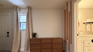 Een kamer met een houten dressoir, een witte deur en een raam met gordijnen.