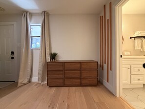 Et værelse med en trækommode, en hvid dør og et vindue med gardiner.