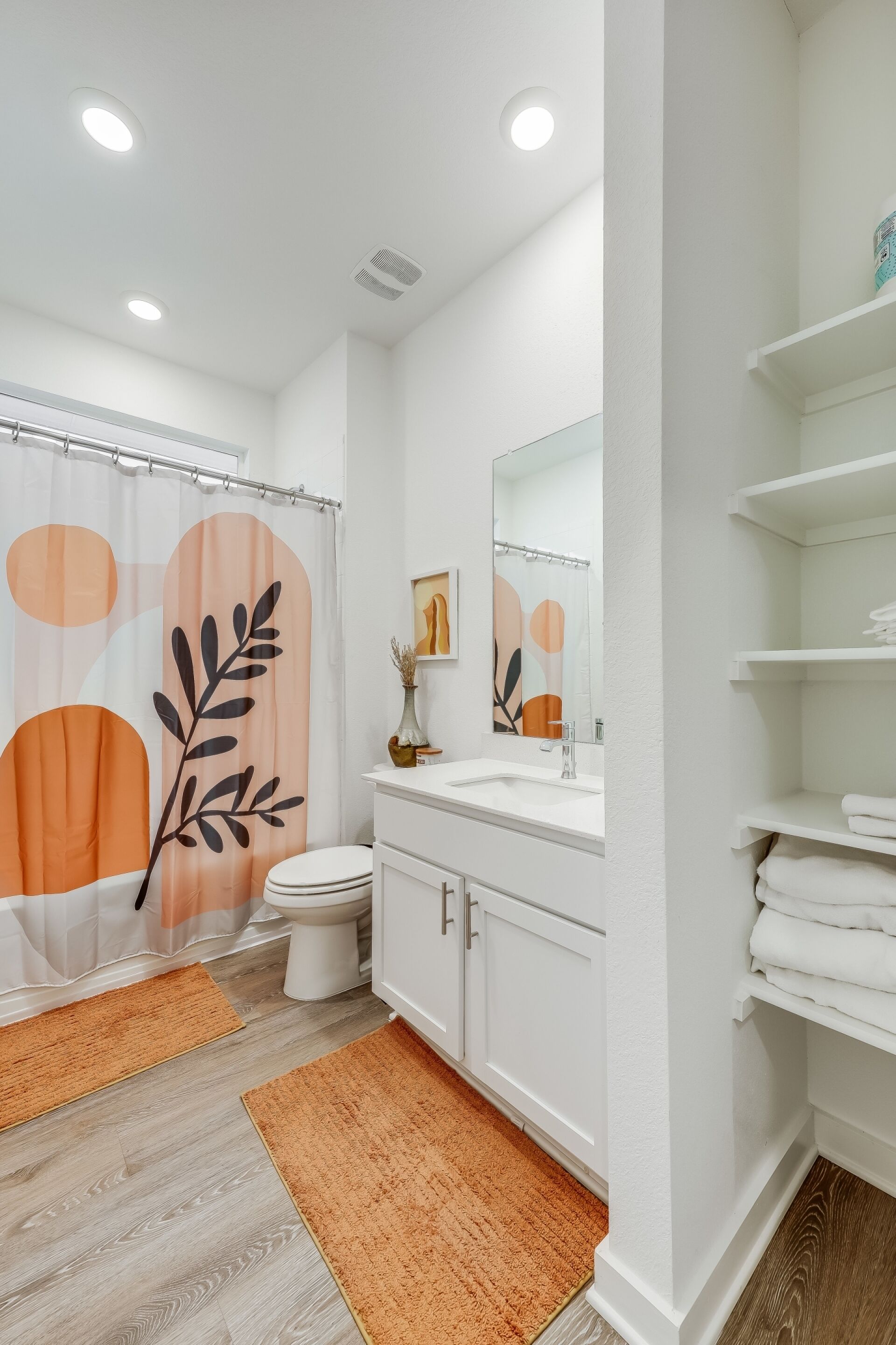 Une salle de bain équipée d’un rideau de douche, de toilettes, d’un lavabo, d’un miroir et d’étagères.