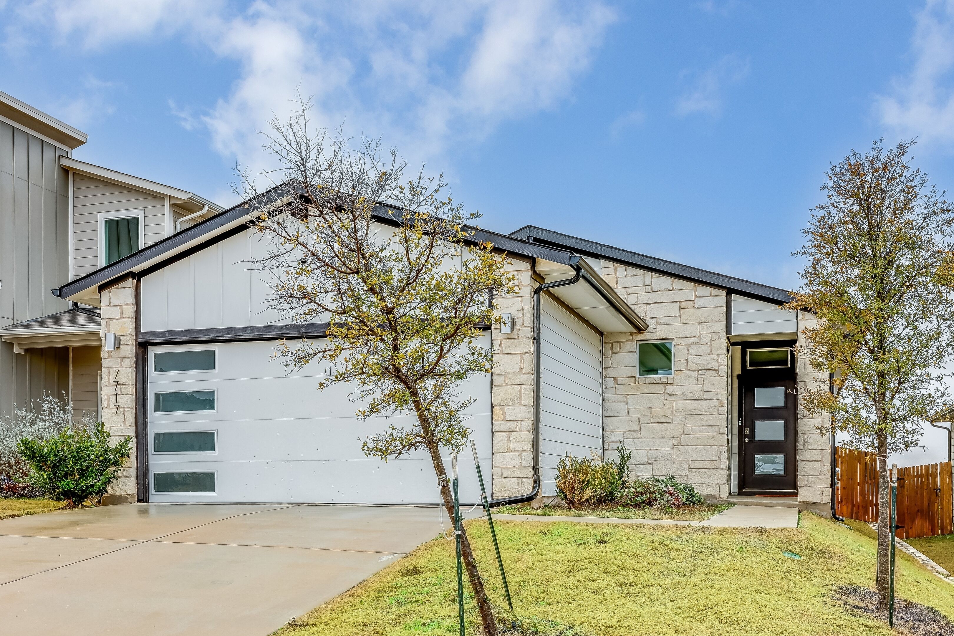 A modern house with a garage, stone exterior, and a small tree in the front yard.
