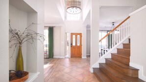 A hallway with a wooden staircase, a door, and a vase with branches. - 5BR Cedar Park | Near HEB Center + Private Yard (Cedar Park)