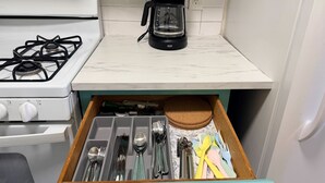 Een keuken met een gasfornuis, een koffiezetapparaat en een lade met keukengerei.