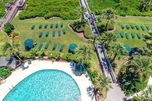 Eine Vogelperspektive eines Resorts mit einem großen Pool, Liegestühlen und einem Weg zu einer Terrasse.