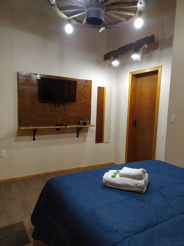 Un dormitorio con cama, televisor montado en un panel de madera, una puerta y un ventilador de techo.