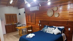 A cozy room with a bed, a wooden headboard, a small table, and a kitchenette. - Aconchego da Serra Geminados (São Joaquim)