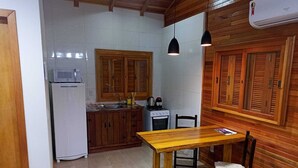 A compact kitchen with wooden cabinets, a white refrigerator, a stove, and a dining table with two chairs. - Aconchego da Serra Geminados (São Joaquim)