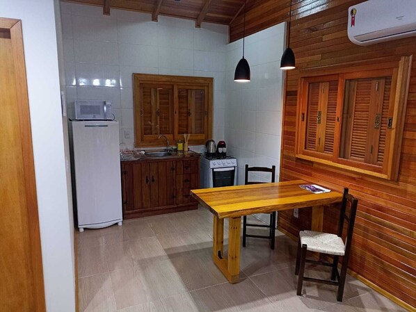 A compact kitchen with wooden cabinets, a white refrigerator, a stove, and a dining table with two chairs.
