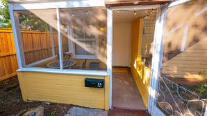 A screened porch with a small table and chairs, a mailbox, and a wooden fence in the background.