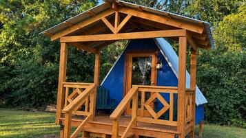 A wooden playhouse with a blue roof and a ramp leading up to the entrance.