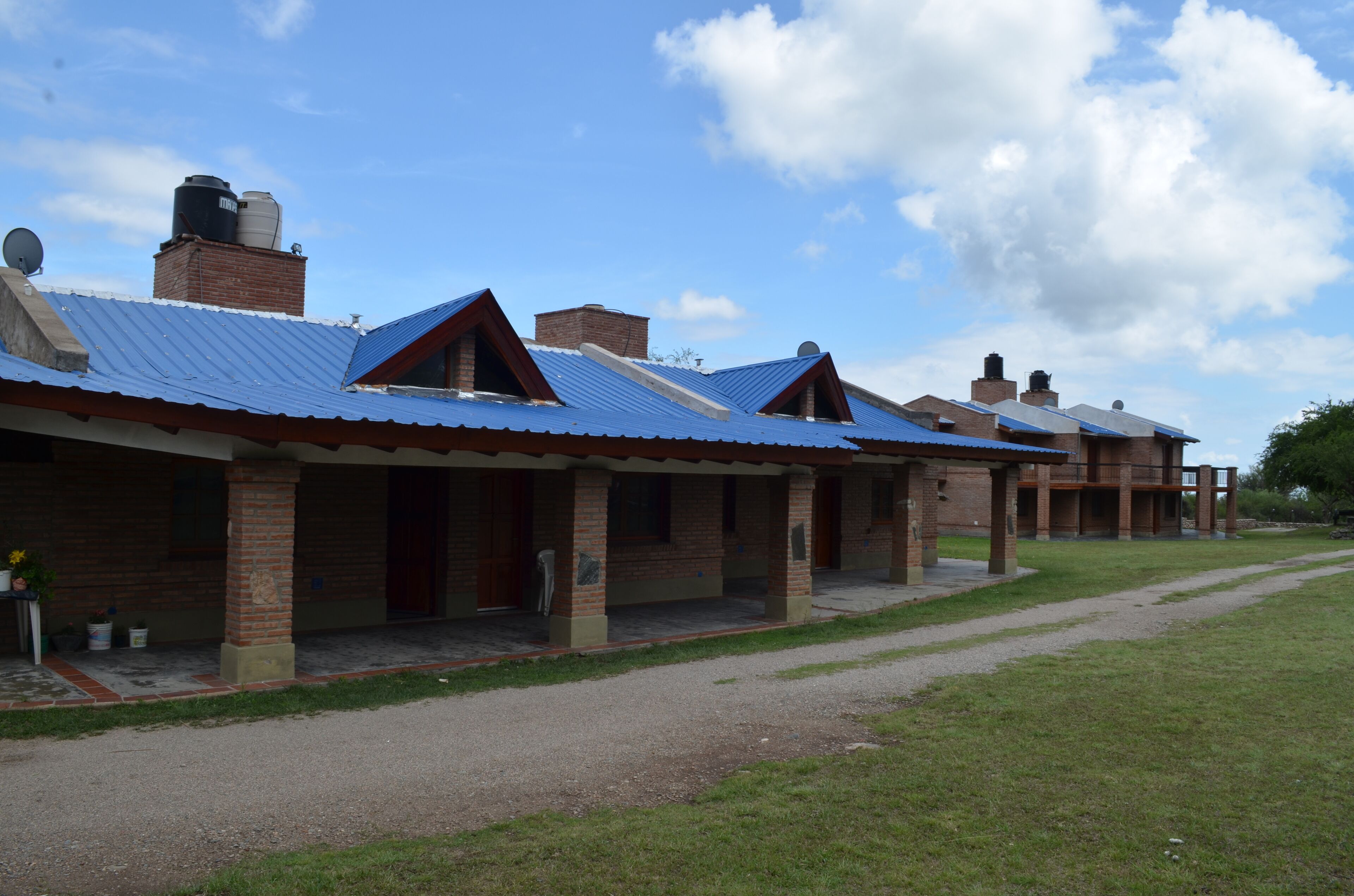 A row of brick buildings with blue roofs and a gravel path leading to them.