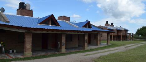 A row of brick buildings with blue roofs and a gravel path leading to them.