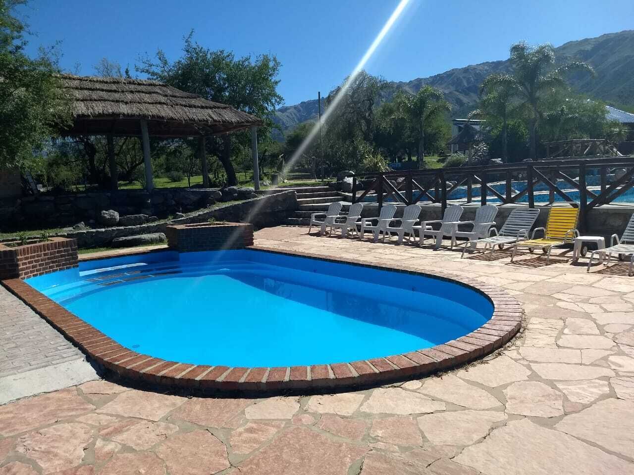 Une piscine bordée de briques, entourée de chaises longues et d’une structure à toit de chaume.