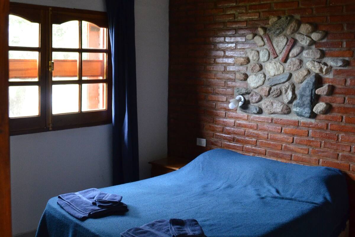 Un dormitorio con cama, ventana con cortinas y pared de ladrillo decorada con piedra.