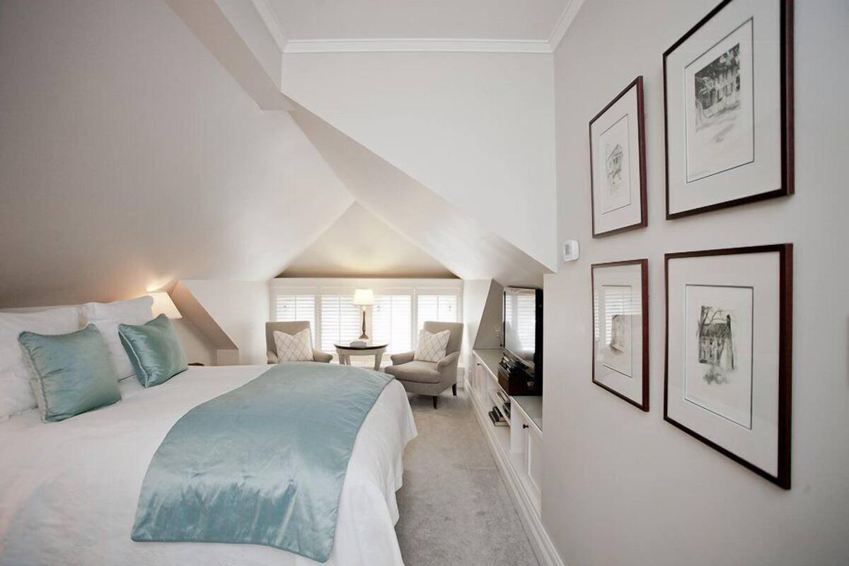 A bedroom with a bed, a desk, and a chair. There are framed pictures on the wall.