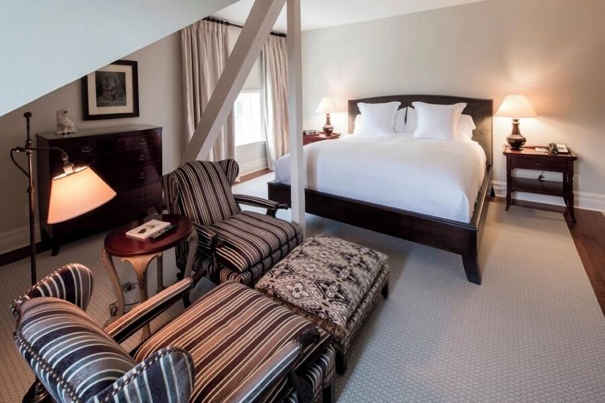 A hotel room with a large bed, a sitting area with striped chairs, a small table, and a lamp.