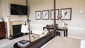Un dormitorio con una cama grande, una chimenea, un escritorio y obras de arte enmarcadas en la pared.