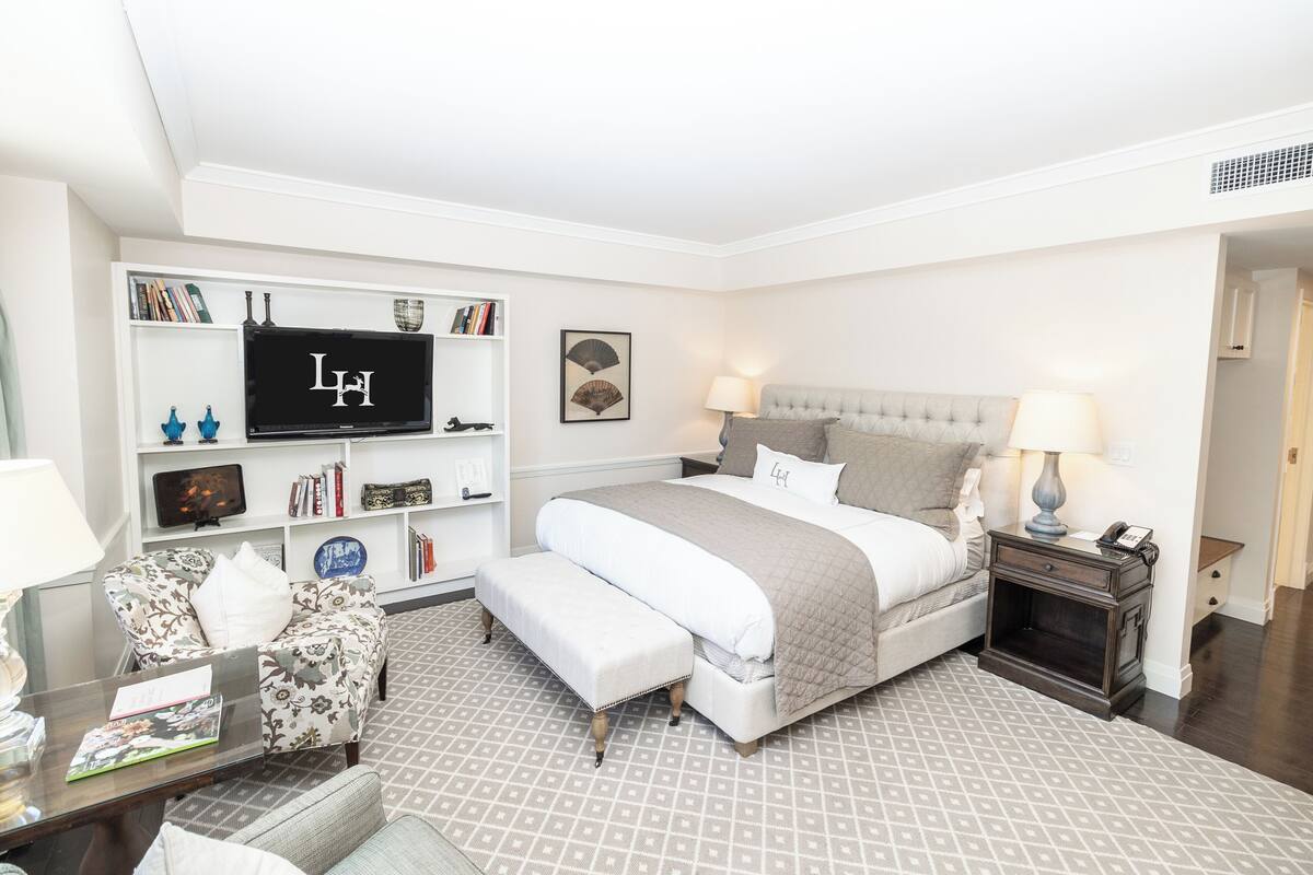 A bedroom with a bed, bedside tables, a TV, a bookshelf, and a patterned rug.