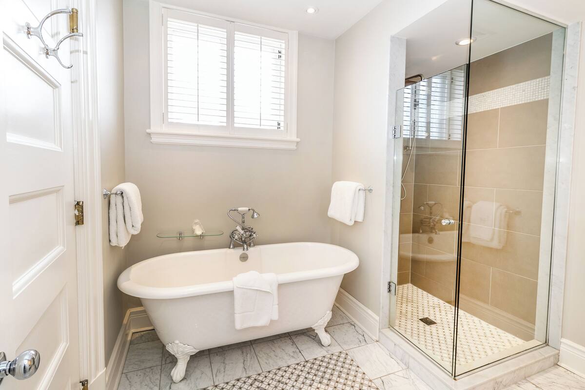 A bathroom with a freestanding bathtub, a glass-enclosed shower, and a window with blinds.