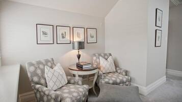A cozy living room with two patterned armchairs, a small round table with books, and framed artwork on the wall.