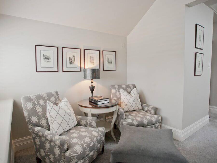 A cozy living room with two patterned armchairs, a small round table with books, and framed artwork on the wall.