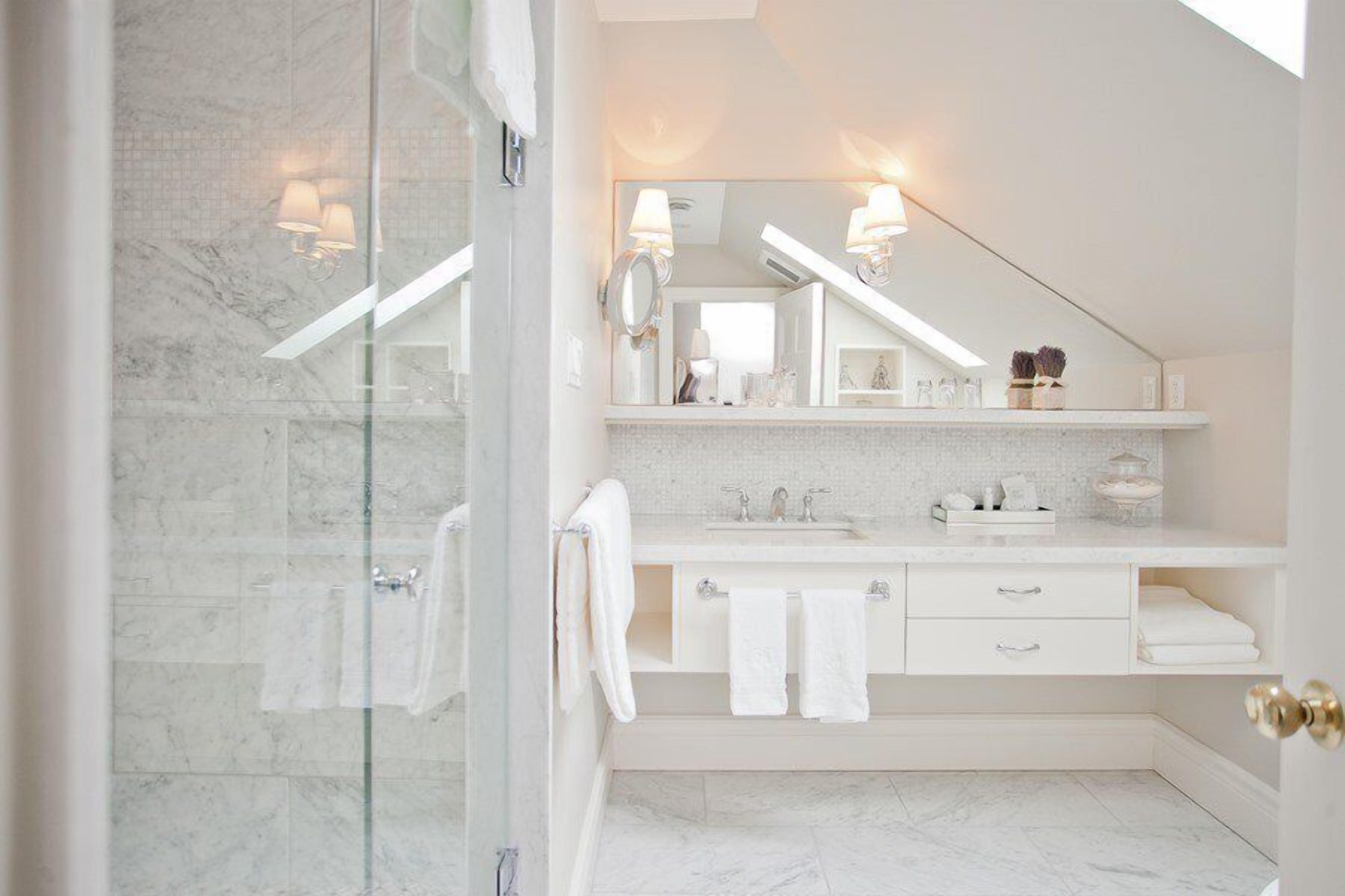 A modern bathroom with a glass shower enclosure, a white vanity with a mirror, and a marble-tiled floor.
